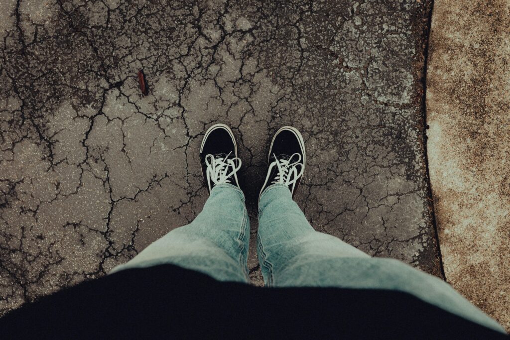 Person wearing casual jeans and sneakers standing on cracked pavement.
